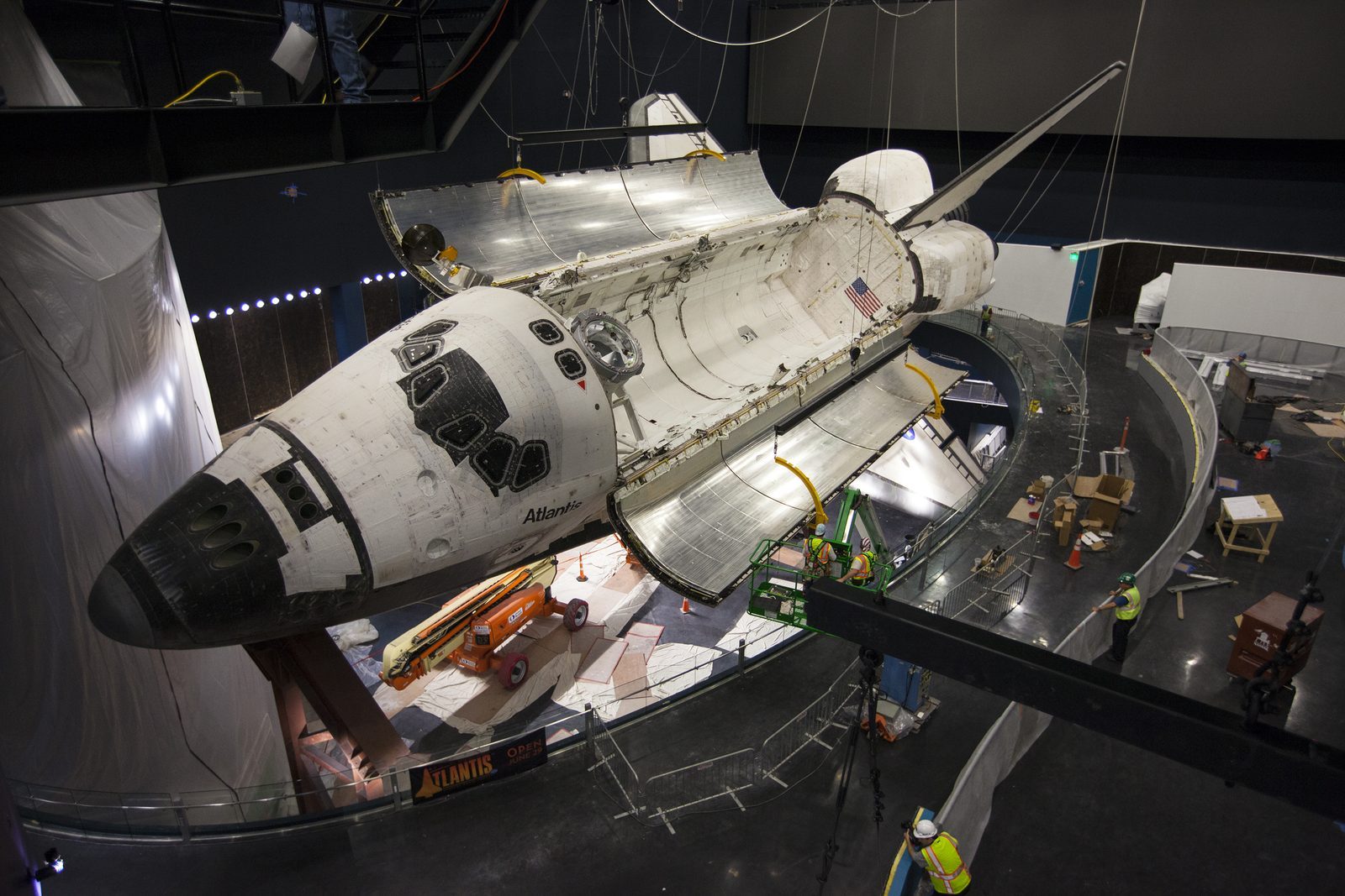 Space shuttle Atlantis displayed tilted inside its exhibit hall at the Kennedy Space Center Visitor Complex, payload bay doors open and robotic arm extended