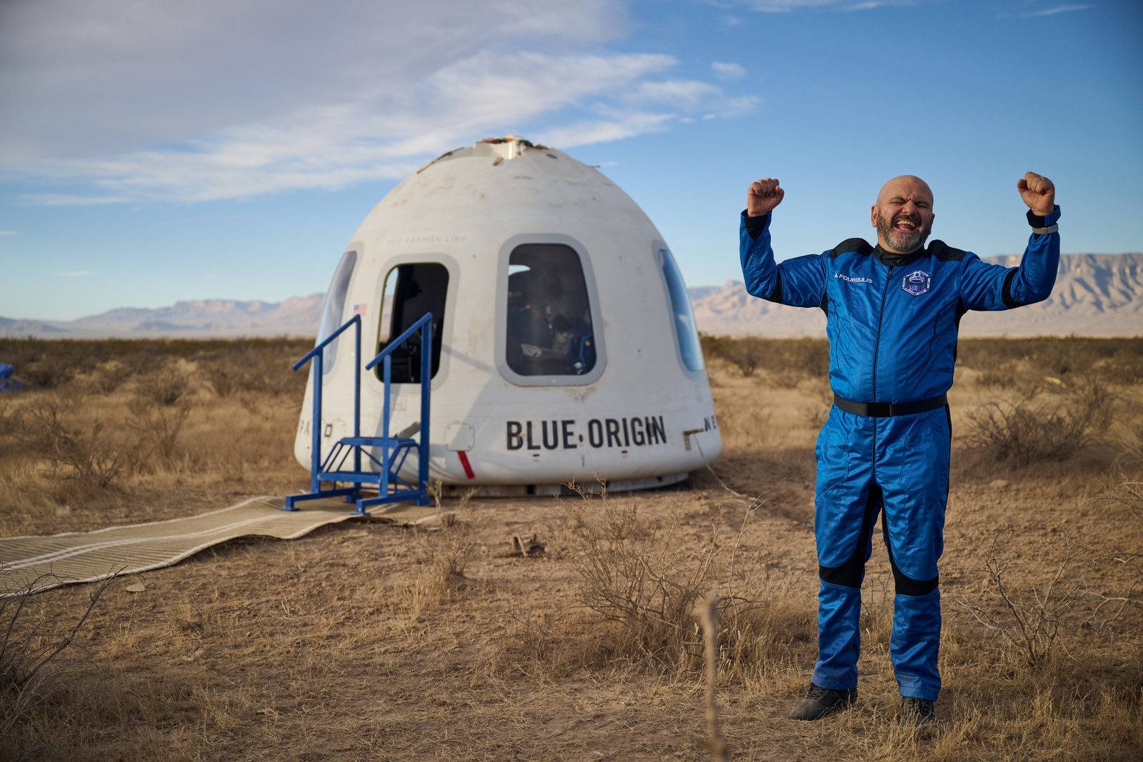 A New Shepard astronaut in Blue Origin's blue flight suit celebrating beside the crew capsule after landing