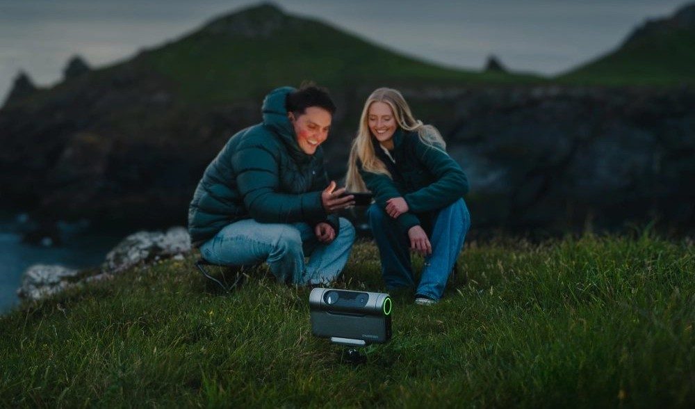 Two stargazers checking a phone beside a DwarfLab Dwarf 3 smart telescope on a starry coastal headland — the smart-scope experience both of these deliver