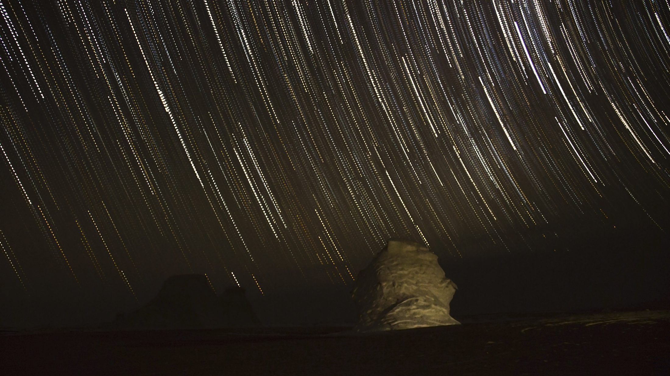 Star trails arc over a pale chalk rock formation in the Egyptian desert at night, stacked from 39 exposures over an hour and a half