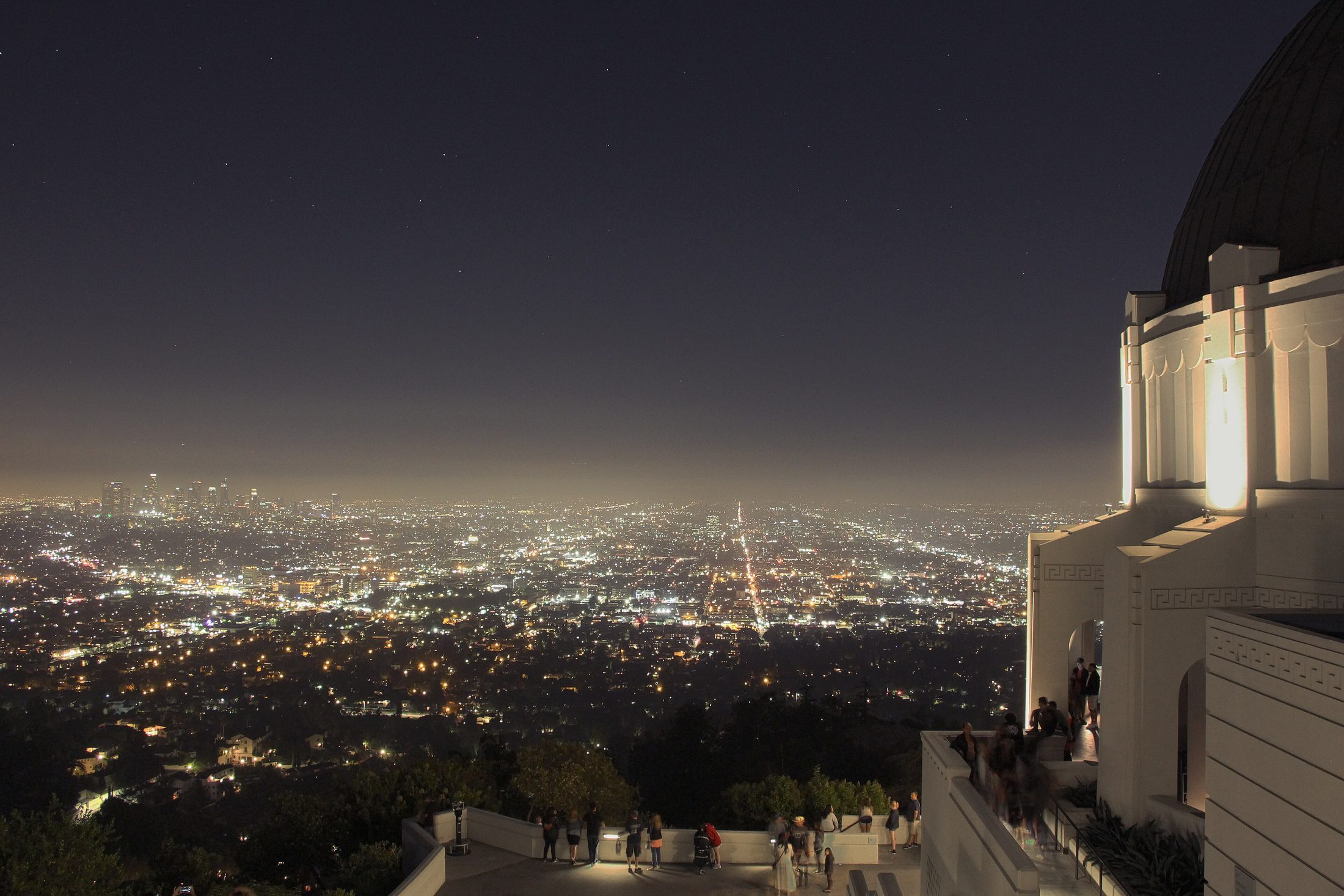 Griffith Observatory lit at night in the foreground, with the Los Angeles skyline and city lights spread out below and stars overhead