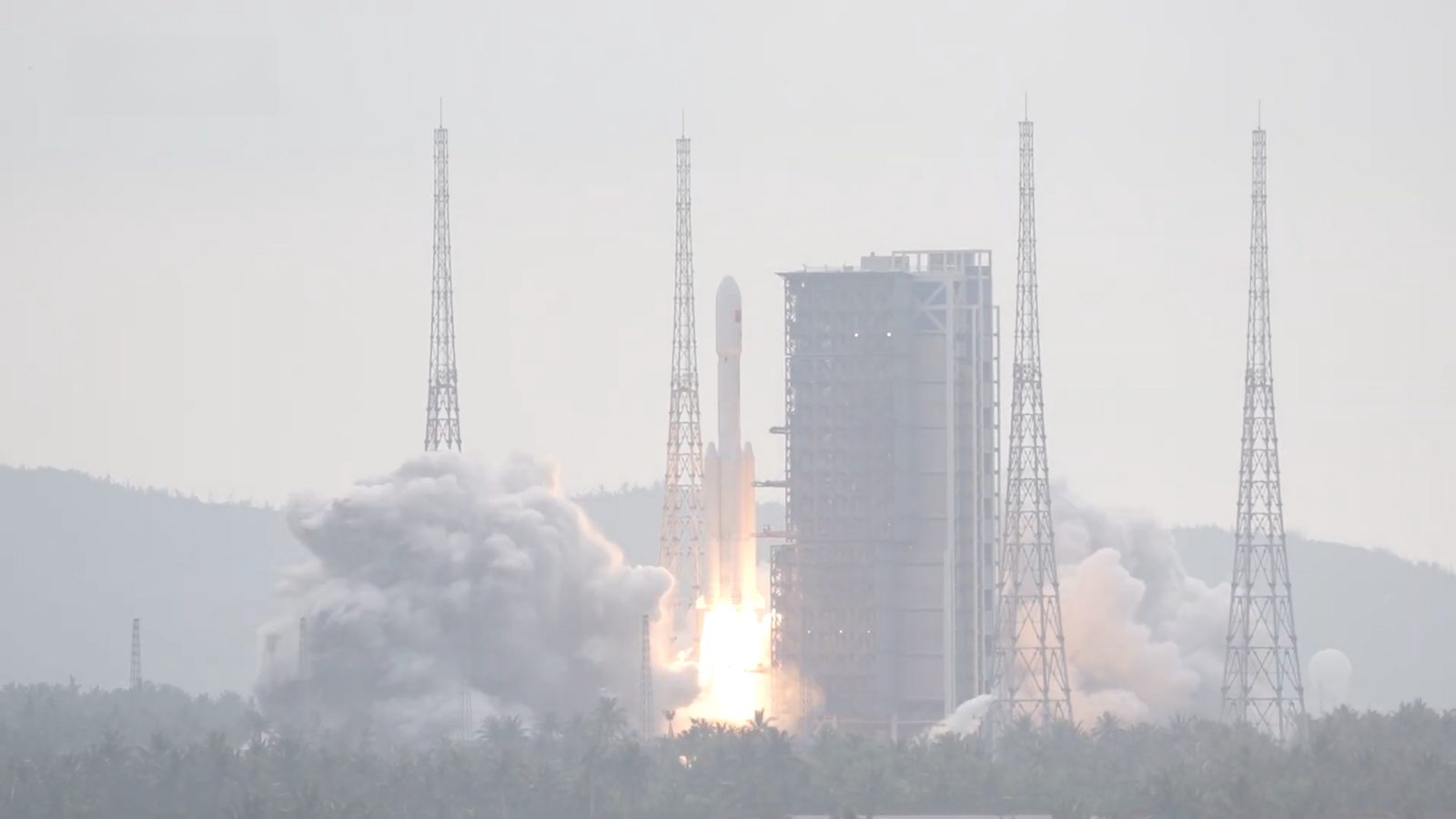 A Long March 7 rocket lifting off in a cloud of exhaust between the lightning towers of its pad at the Wenchang Space Launch Site on Hainan