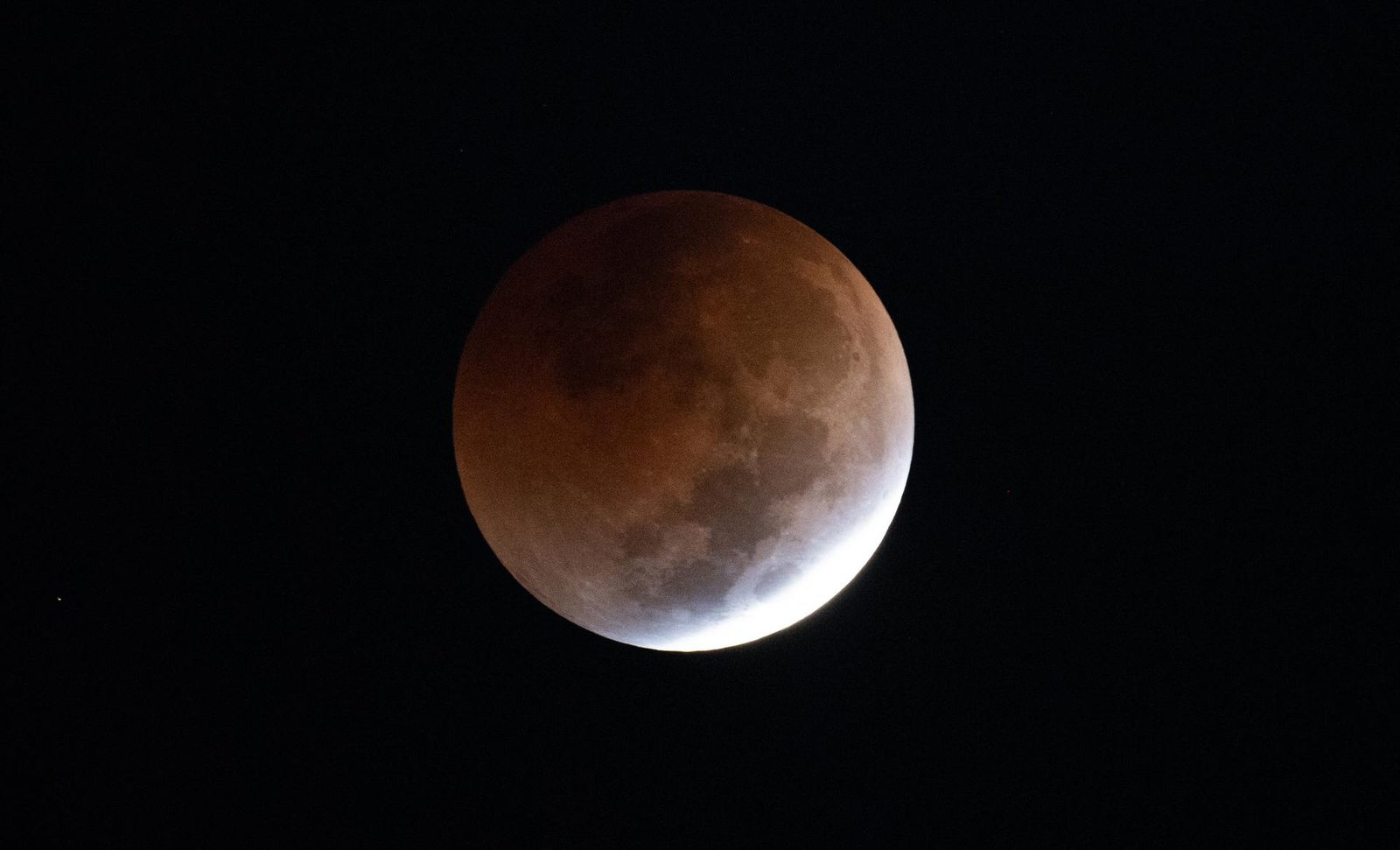 The Moon nearly swallowed by Earth&rsquo;s shadow &mdash; the disc glowing copper red with one bright sliver still in direct sunlight