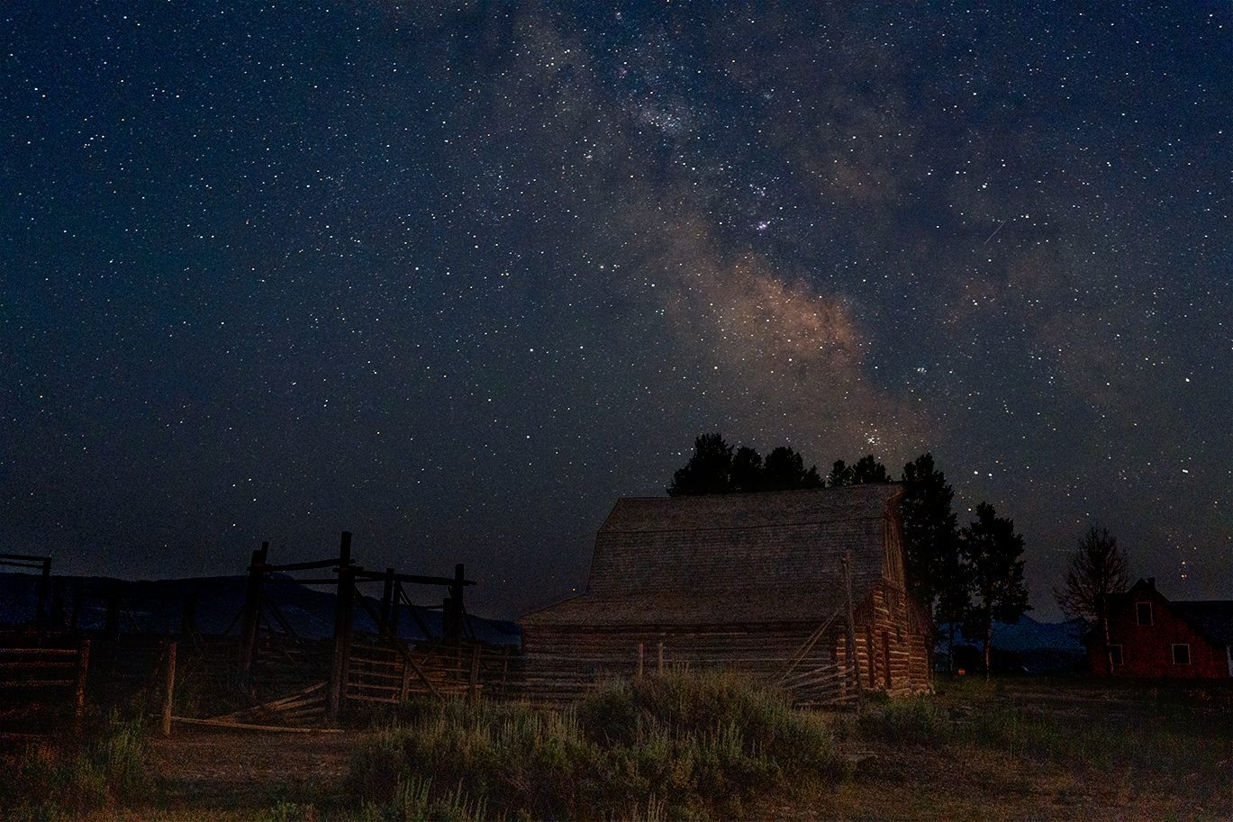 The Milky Way rising over a weathered log barn and wooden corral on Mormon Row in Grand Teton National Park