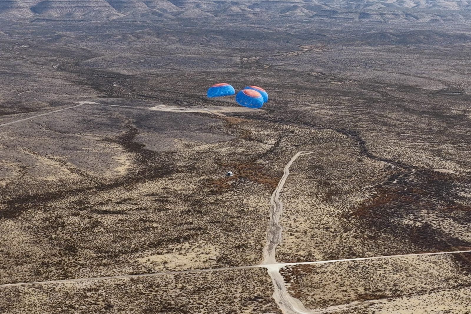 The New Shepard crew capsule descending under three parachutes over the West Texas desert