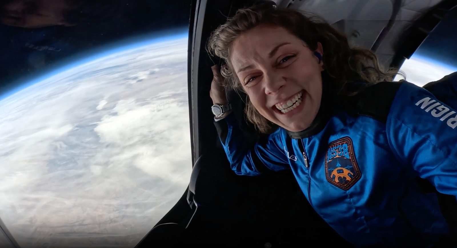 A New Shepard passenger weightless at the top of a suborbital flight, Earth’s curve beyond the window