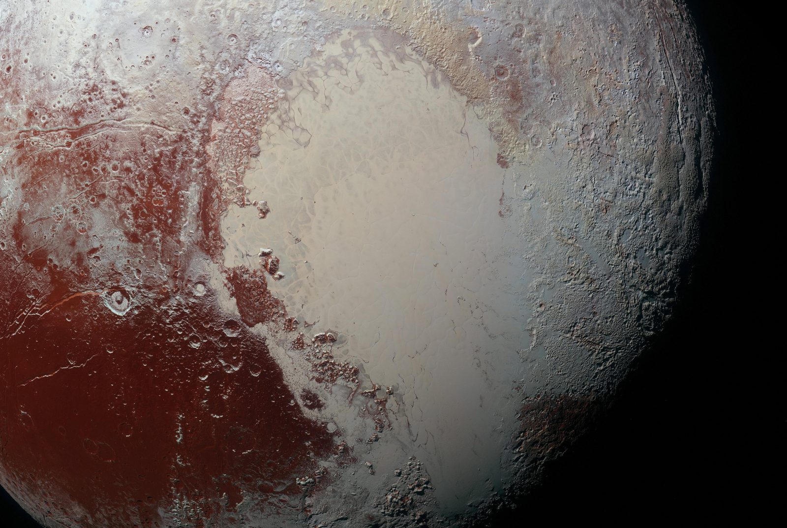 Sputnik Planitia, the bright western lobe of Pluto&rsquo;s heart, in enhanced color &mdash; the smooth nitrogen-ice plain meeting dark red cratered highlands, with mountain blocks standing along its shoreline