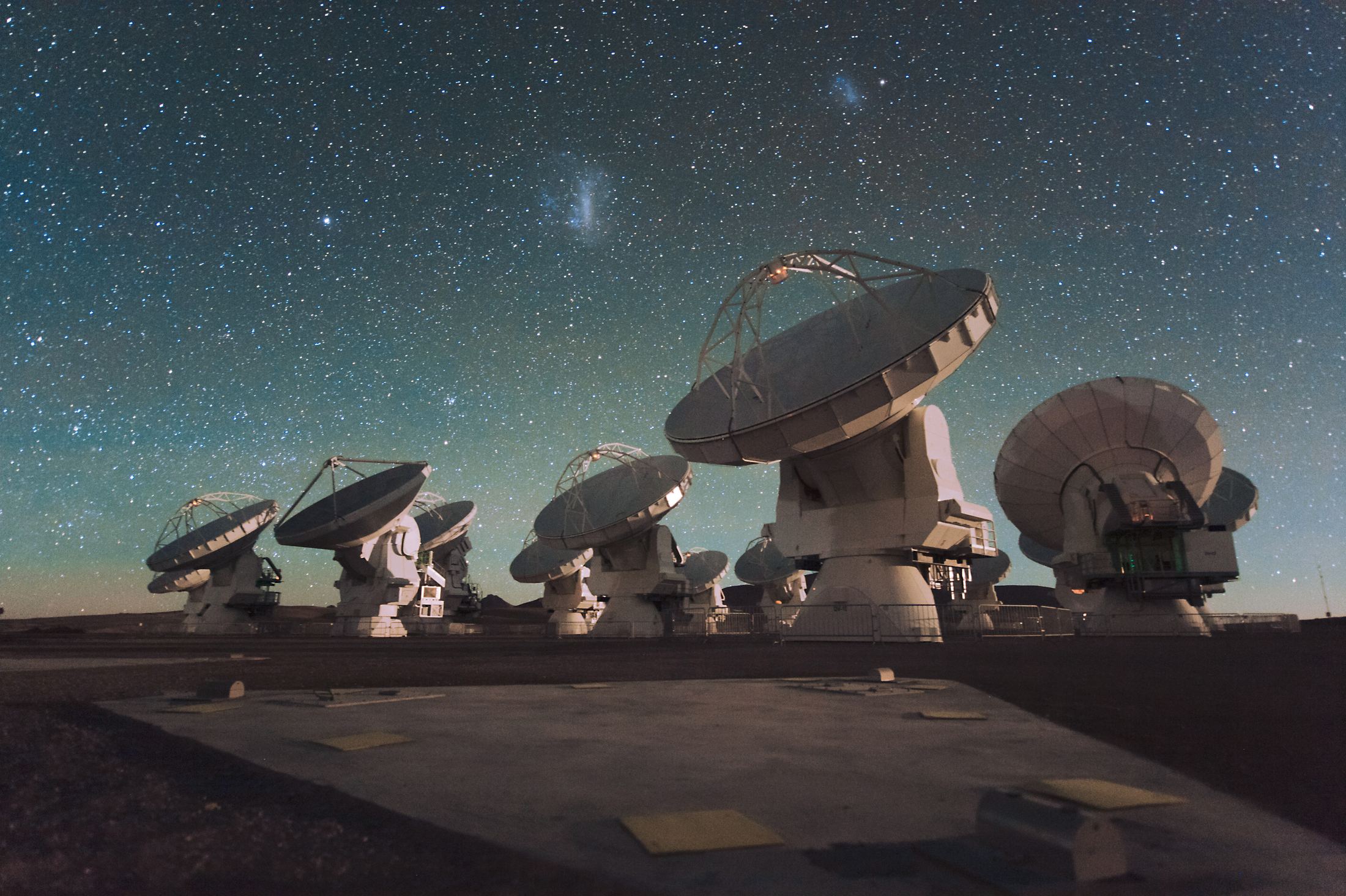 Radio telescope dishes of the ALMA array at night under the Magellanic Clouds