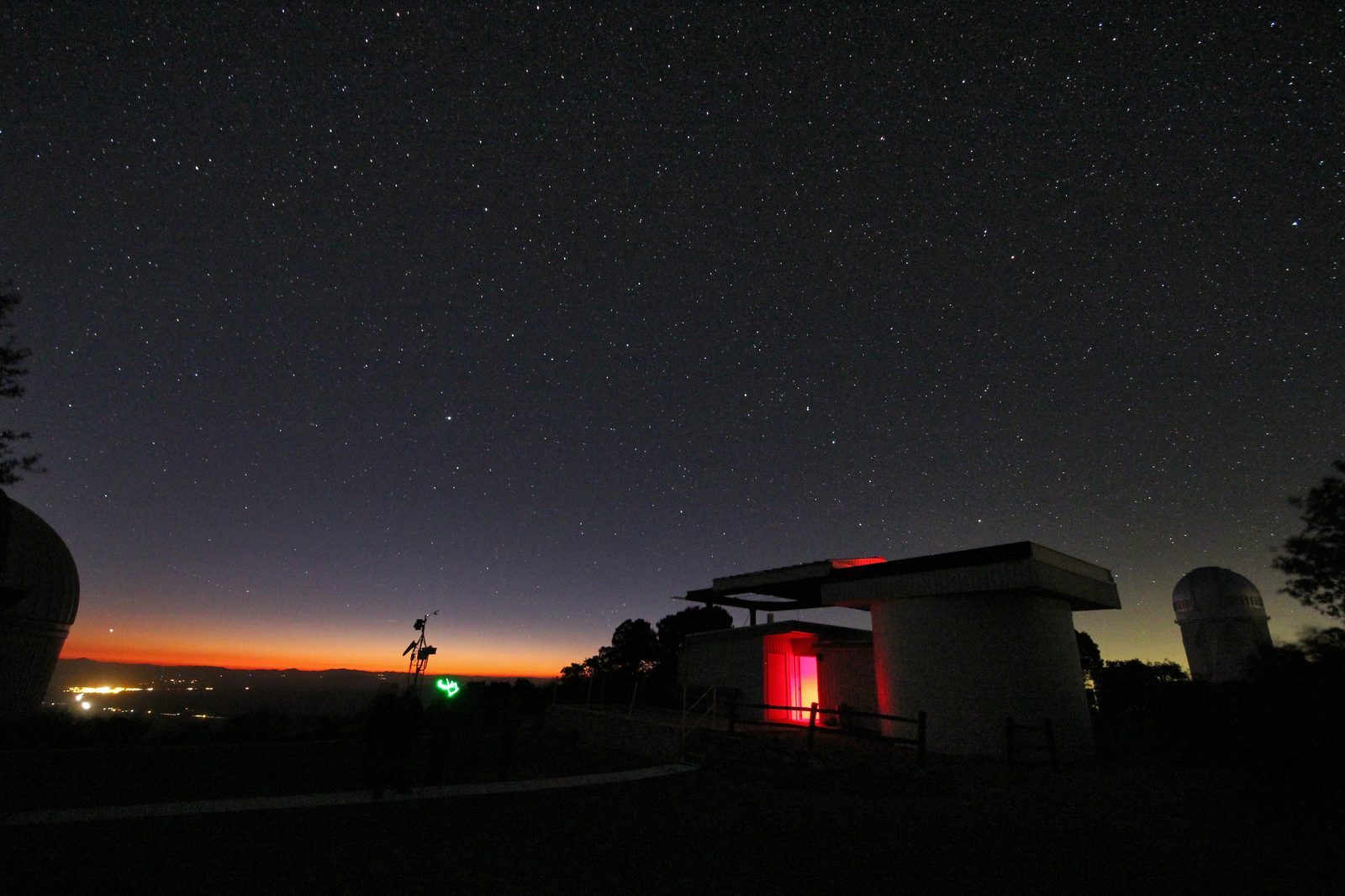 A small roll-off-roof observatory at night, its roof rolled back and its interior glowing red beneath a star-filled sky