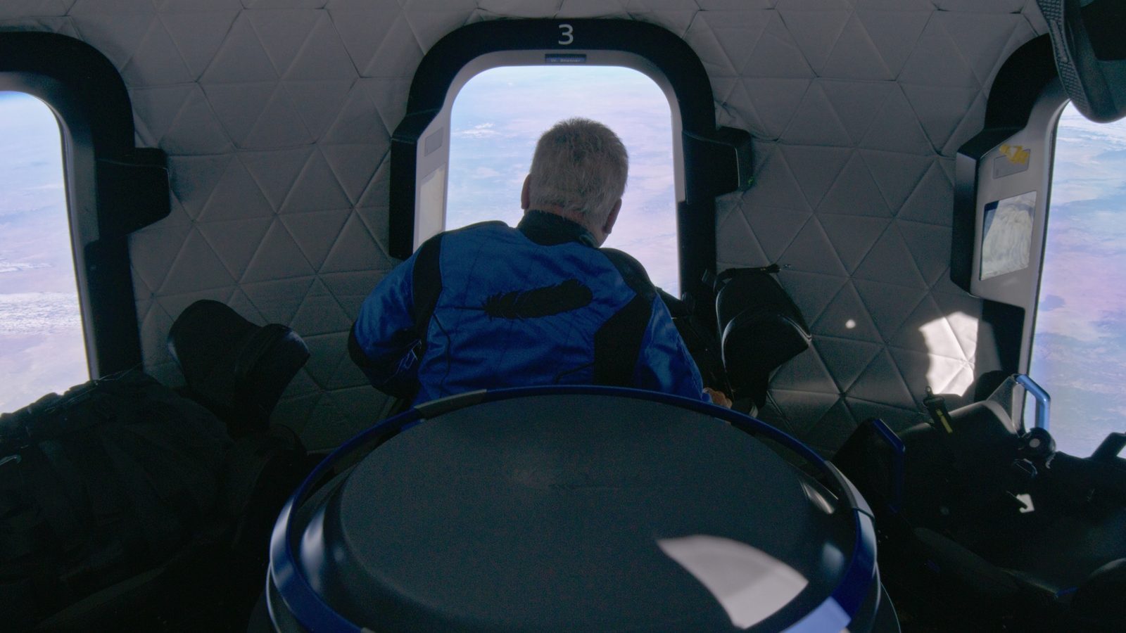 Passengers floating at the windows of a New Shepard capsule at apogee, Earth's curve below