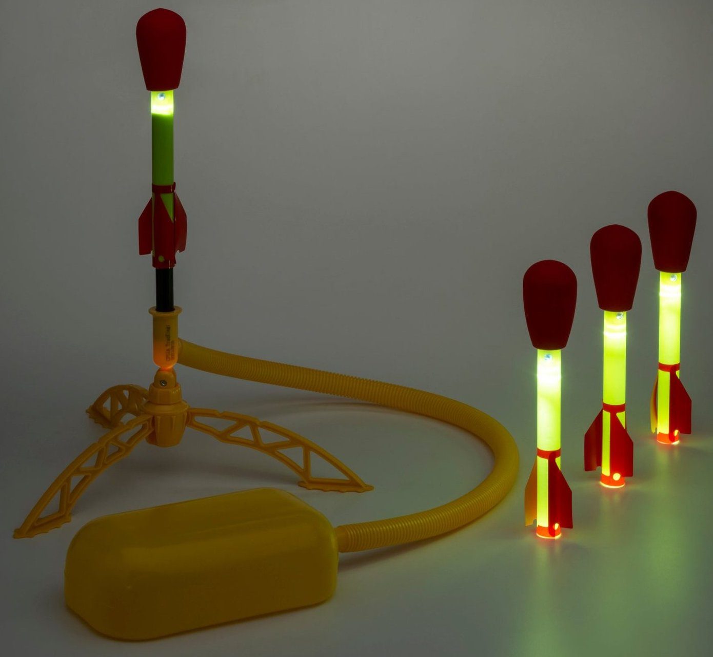 Stomp Rocket Ultra LED launcher with its yellow stomp pad and hose, one rocket on the launch stand and three more beside it, their tubes glowing green