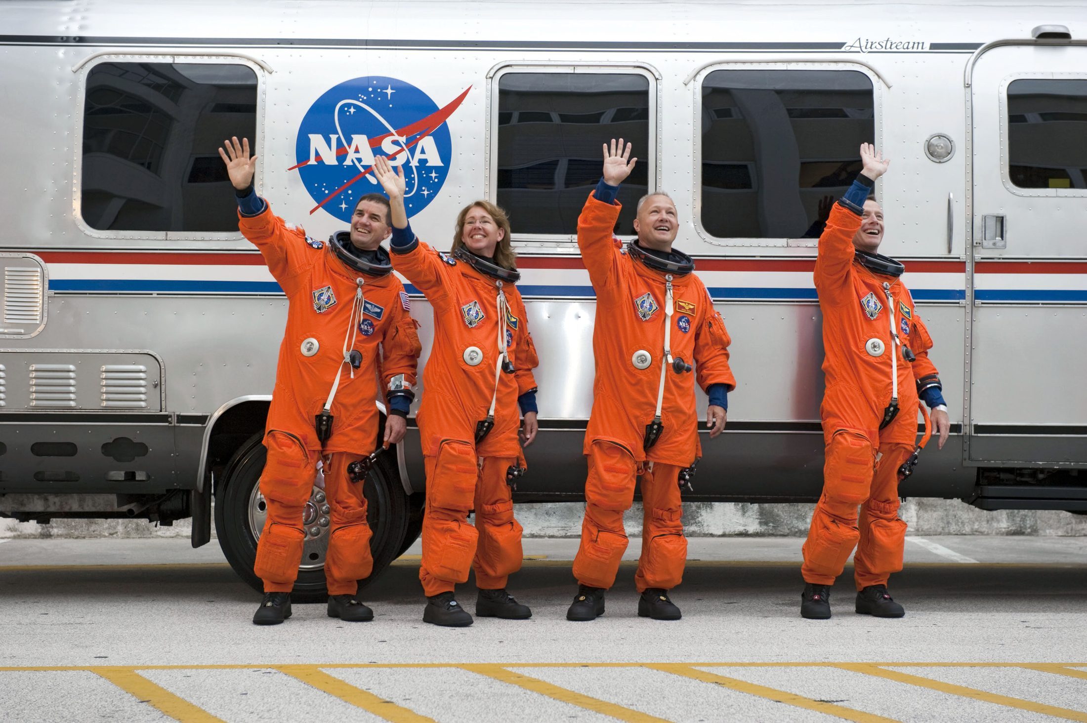 The four STS-135 astronauts waving in bright orange launch-and-entry suits on launch day — the suit every orange astronaut costume is copying
