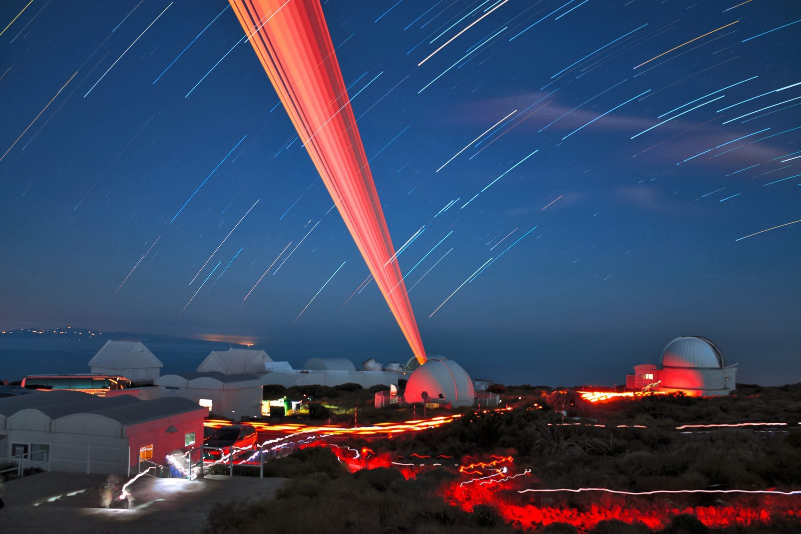 Star trails over the domes of the Teide Observatory on Tenerife, with a red laser beam pointing skyward during a long exposure