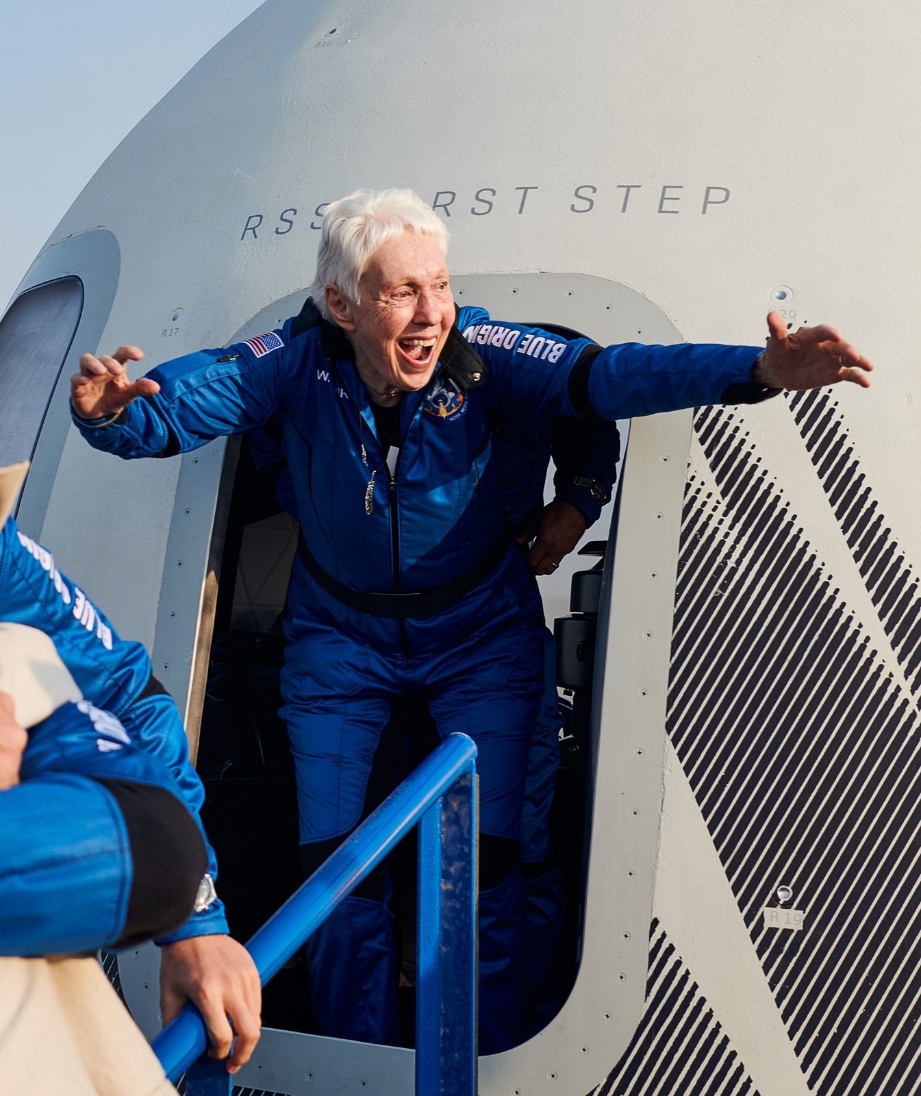 Wally Funk emerging from the New Shepard crew capsule with her arms spread wide after her first flight to space