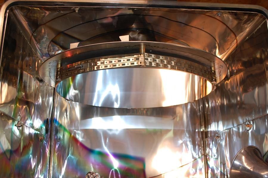Inside the Zambuto Optical vacuum coating chamber: a 25-inch mirror in its ring, just coated, surrounded by rippled foil walls
