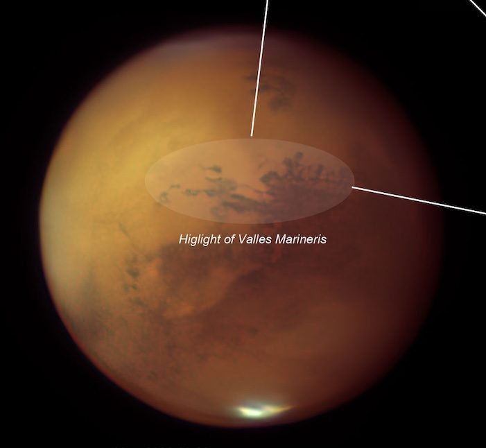 Mars in orange-red with dark surface markings and a bright polar cap, with a pointer and label highlighting the Valles Marineris canyon system, photographed through a 12.5-inch Zambuto mirror